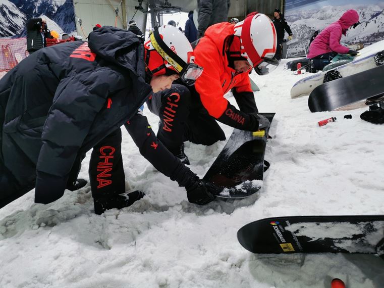 图为比赛间隙教练员和运动员为雪板打蜡